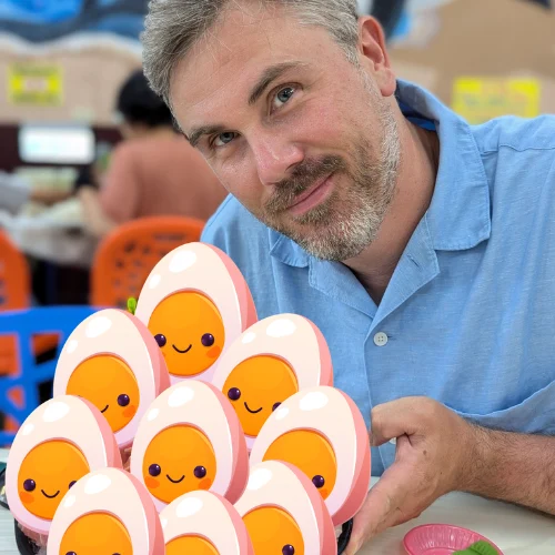 A smiling man in blue shirt presenting a plate of cartoon boiled eggs.